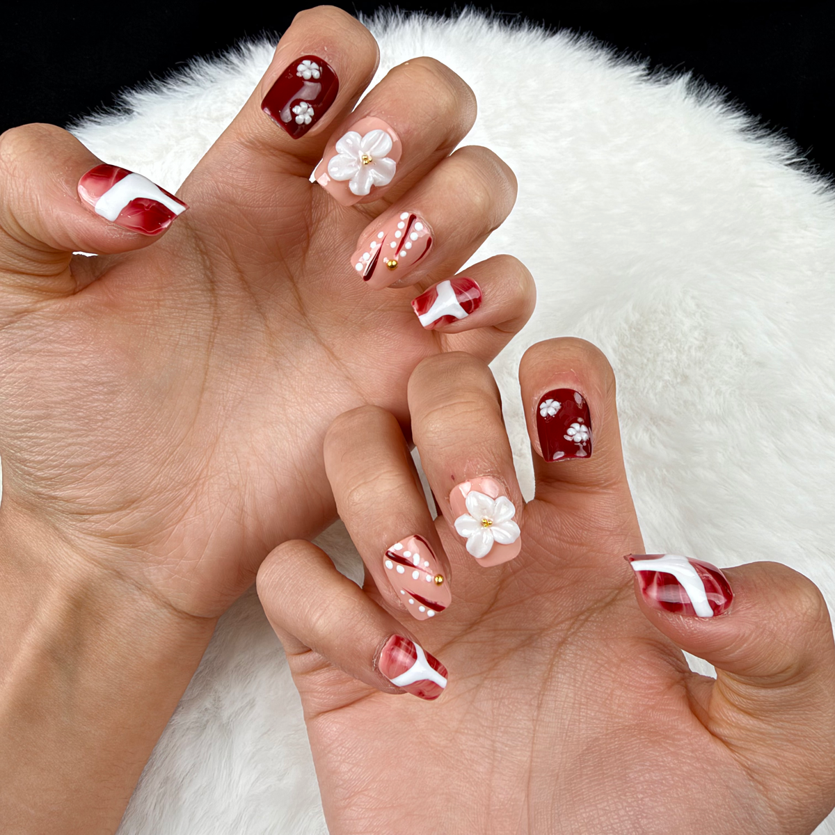 Close-up of hands wearing Burgundy Blossom burgundy and nude floral square press-on nails with white flowers