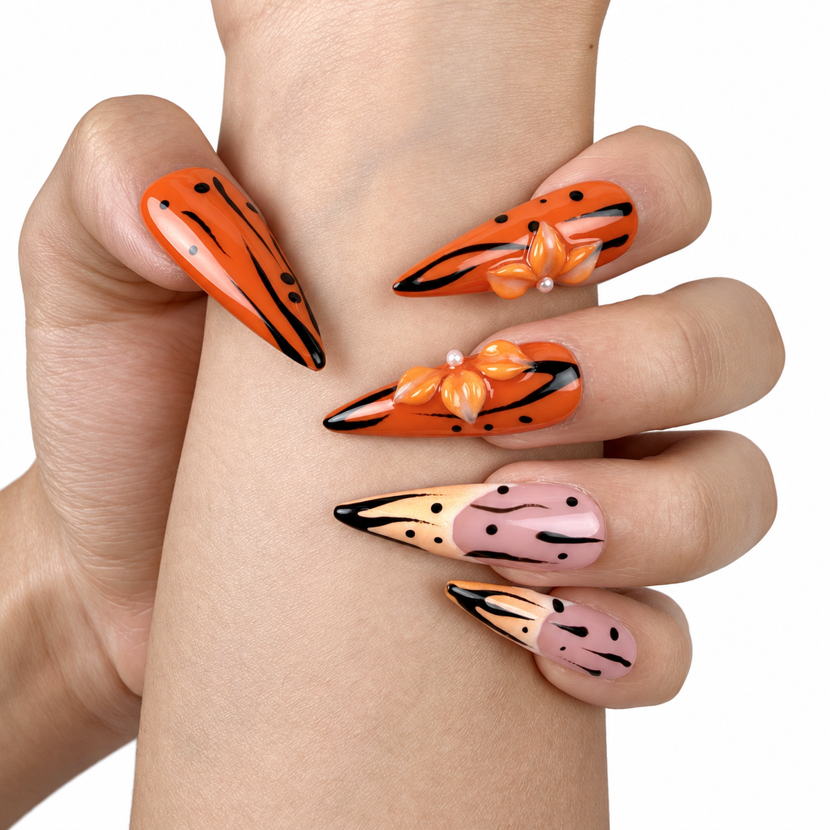 Detail shot of Tangerine Edge orange chrome and nude pink stiletto press-on nails with black floral details on hand