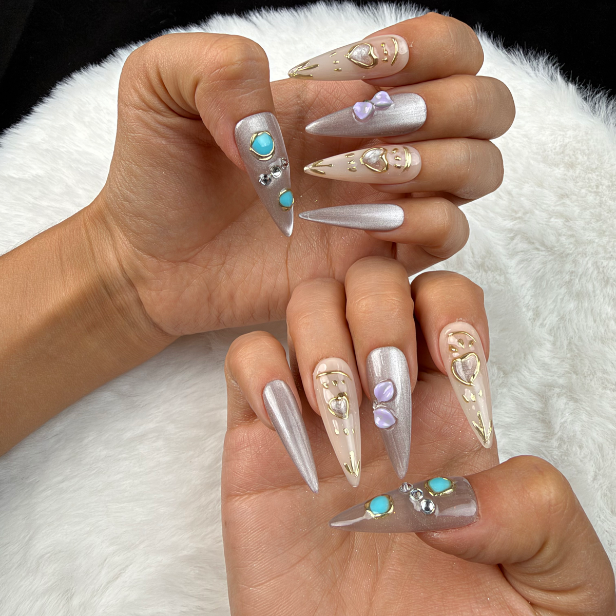 Hands wearing Silver Muse silver chrome stiletto press-on nails with turquoise stones and a heart charm