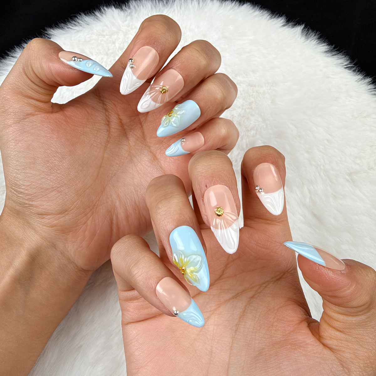 Close-up of hands wearing Seaside Petals light blue and nude shell floral almond press-on nails