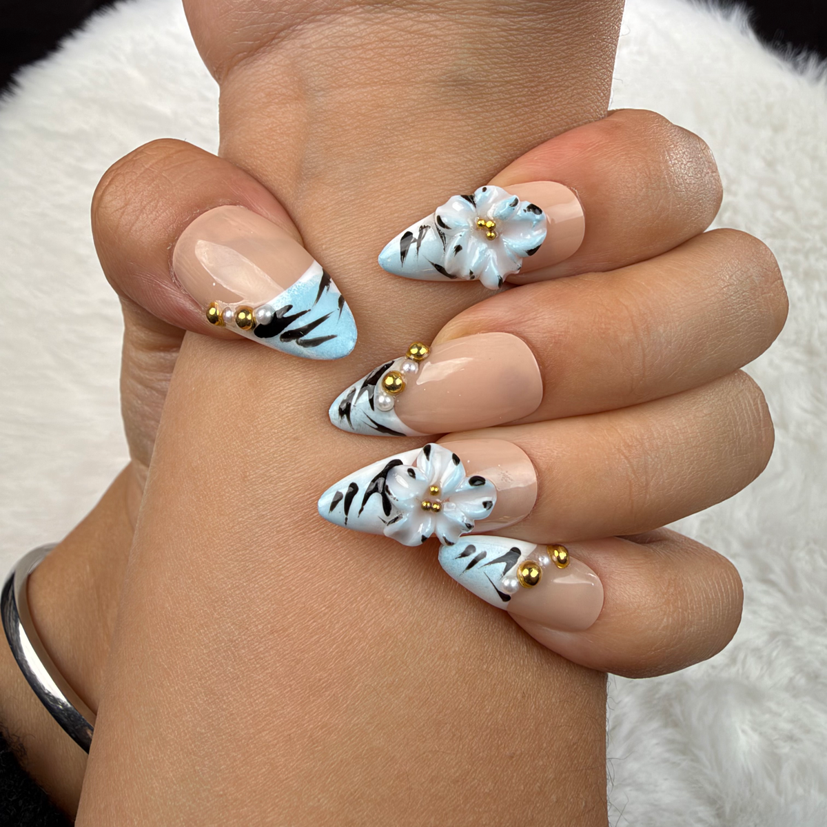 Close-up of hands wearing Frost Bloom ice blue striped French tip almond press-on nails with white flowers