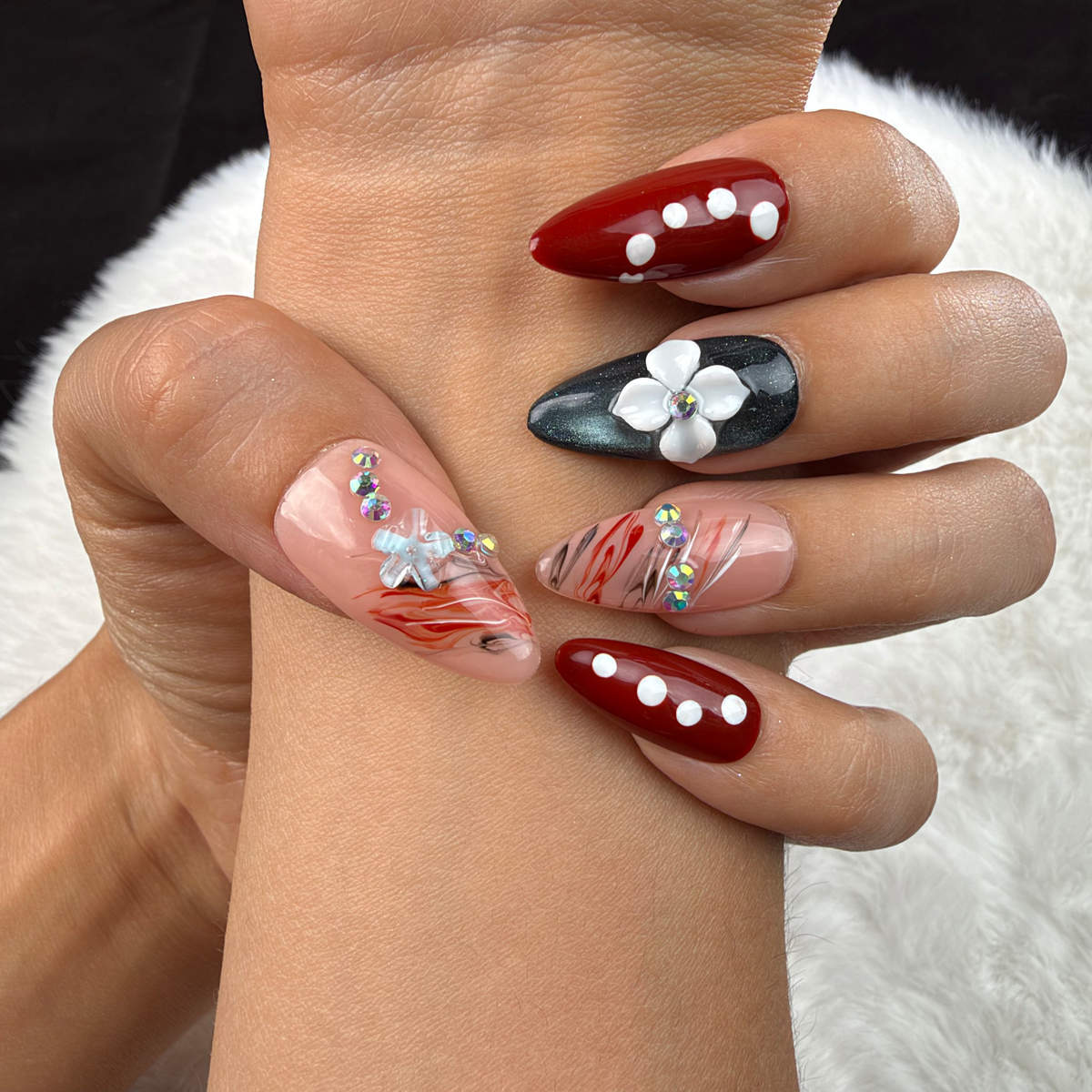 Close-up of hands wearing Ruby Petal red and black floral almond press-on nails with rhinestones