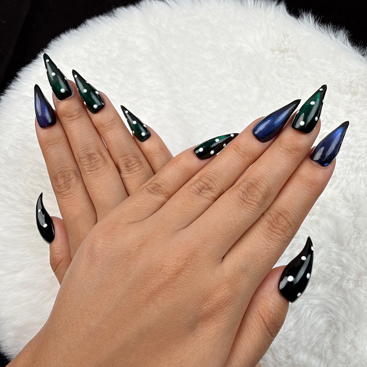 Hands wearing Emerald After Dark green and blue cat eye stiletto press-on nails with rhinestones