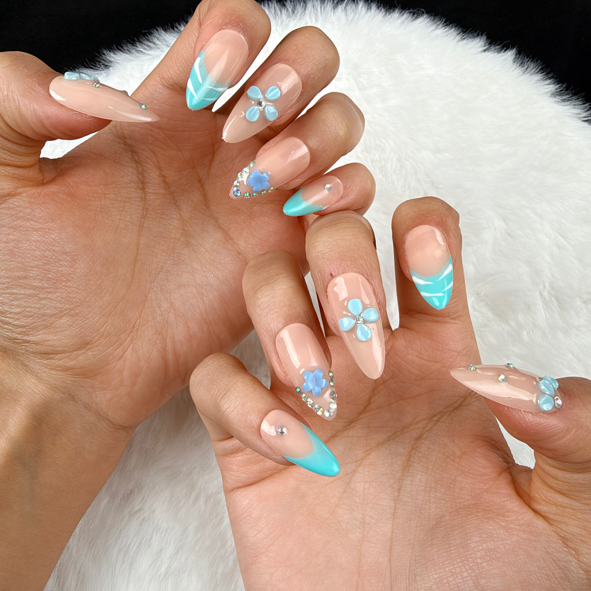 Close-up of hands wearing Aqua Blossom turquoise French tip and blue floral almond press-on nails