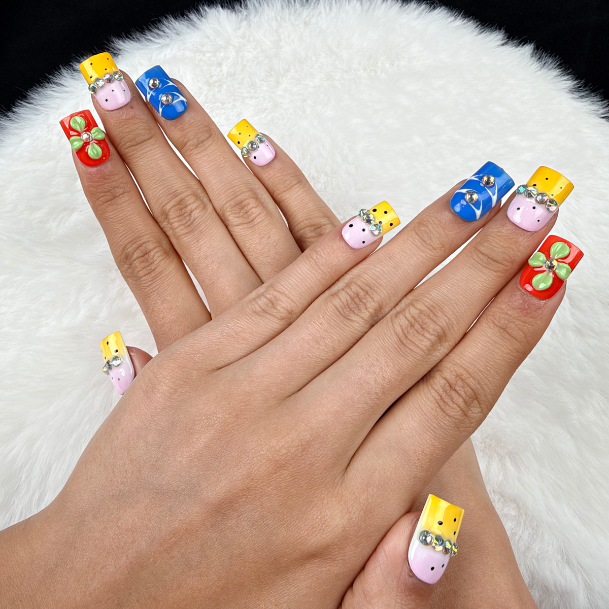 Hands wearing Colour Parade yellow, pink and blue floral square press-on nails