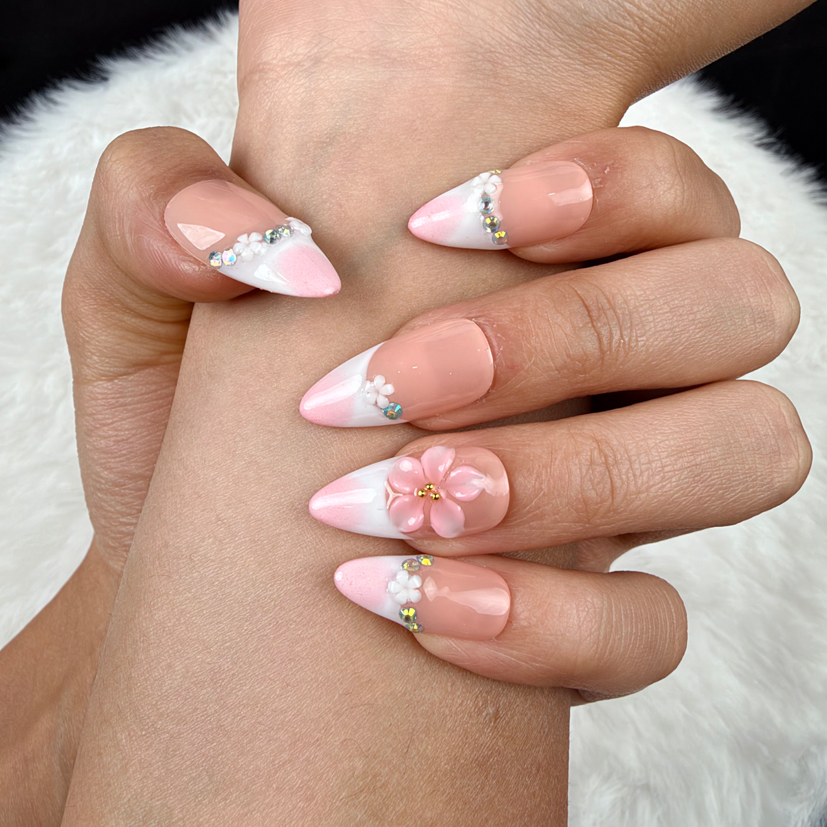 Detail shot of Blush Tiara pink French tip press-on nails with sparkle and floral accents on hand