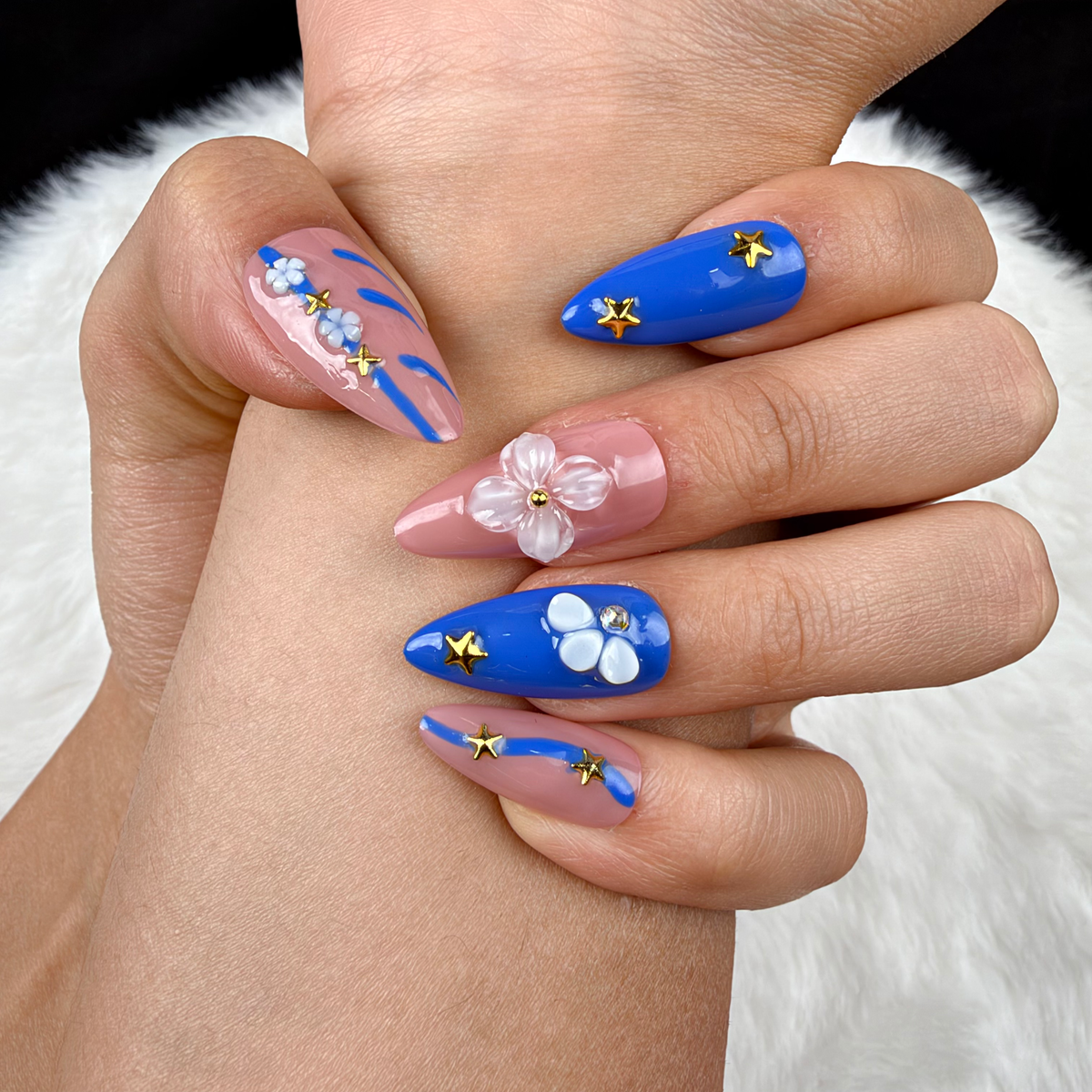 Detail shot of Blue Starlight cobalt blue and pink floral star almond press-on nails on hand