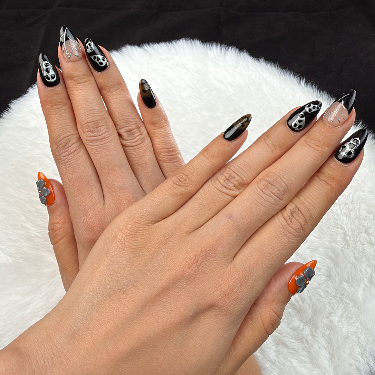 Detail shot of Midnight Web black and orange skull and spiderweb almond press-on nails on hand
