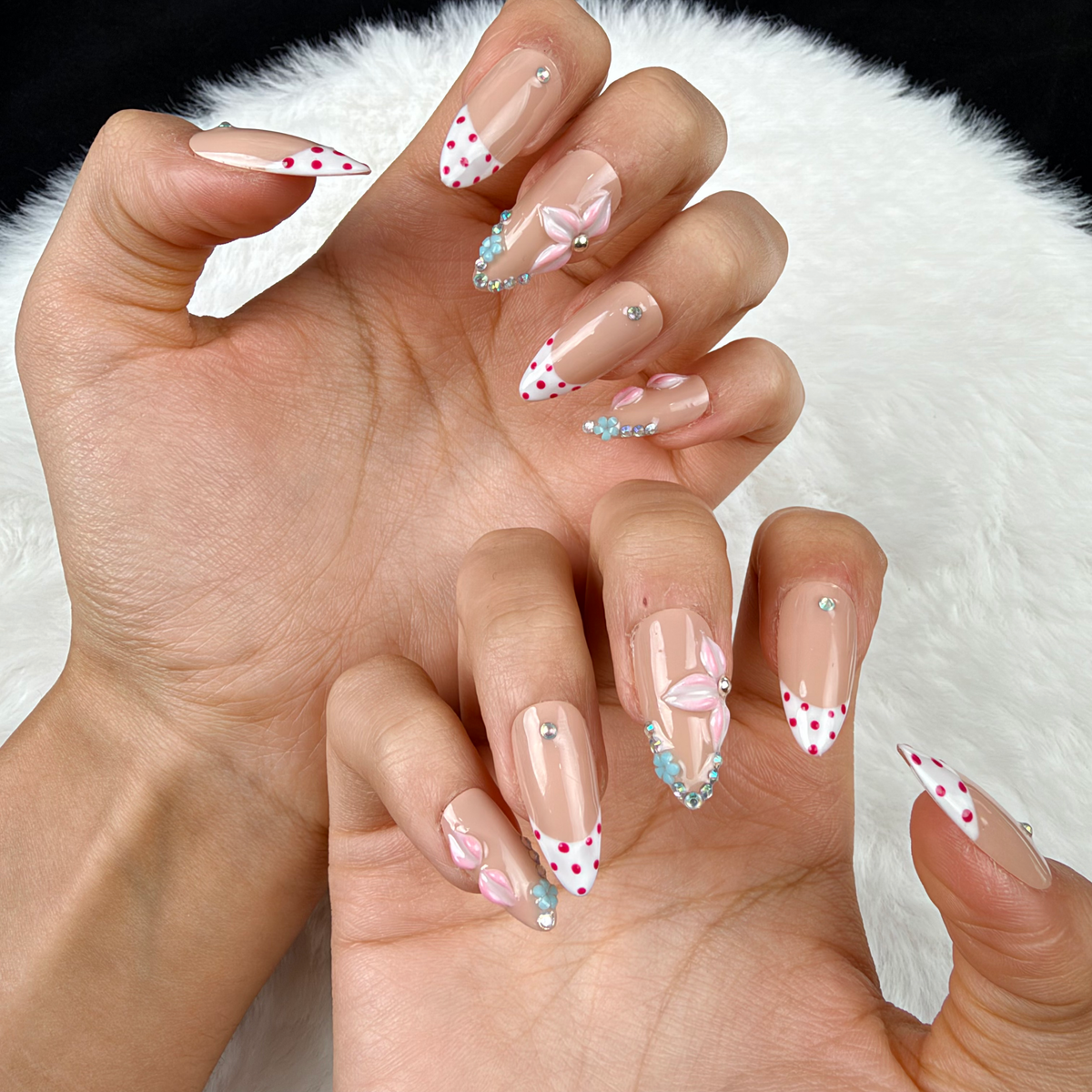 Close-up of hands wearing Blush Garland pink polka dot French tip floral almond press-on nails