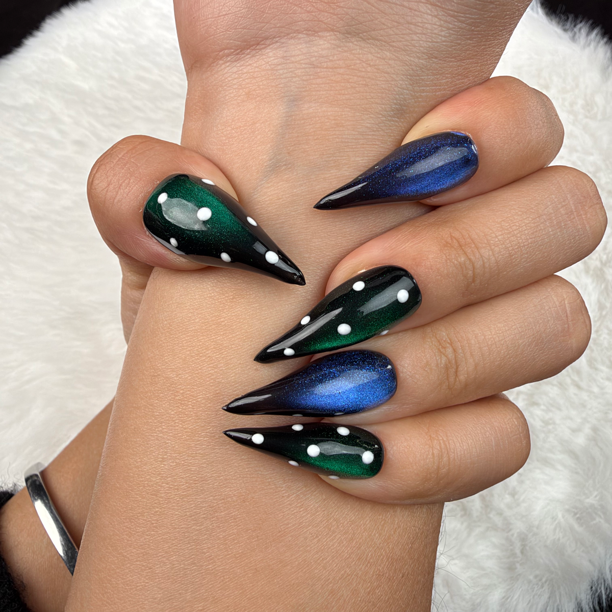 Close-up of hands wearing Emerald After Dark green and blue cat eye stiletto press-on nails with rhinestones