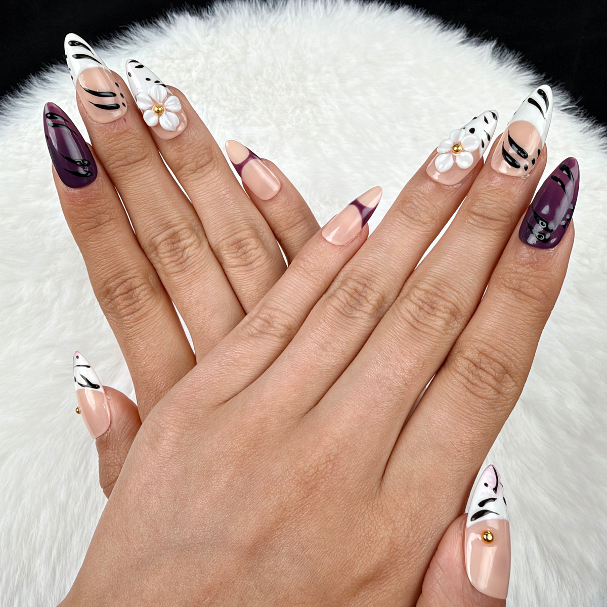 Hands wearing Plum Safari plum, black and white zebra print floral almond press-on nails