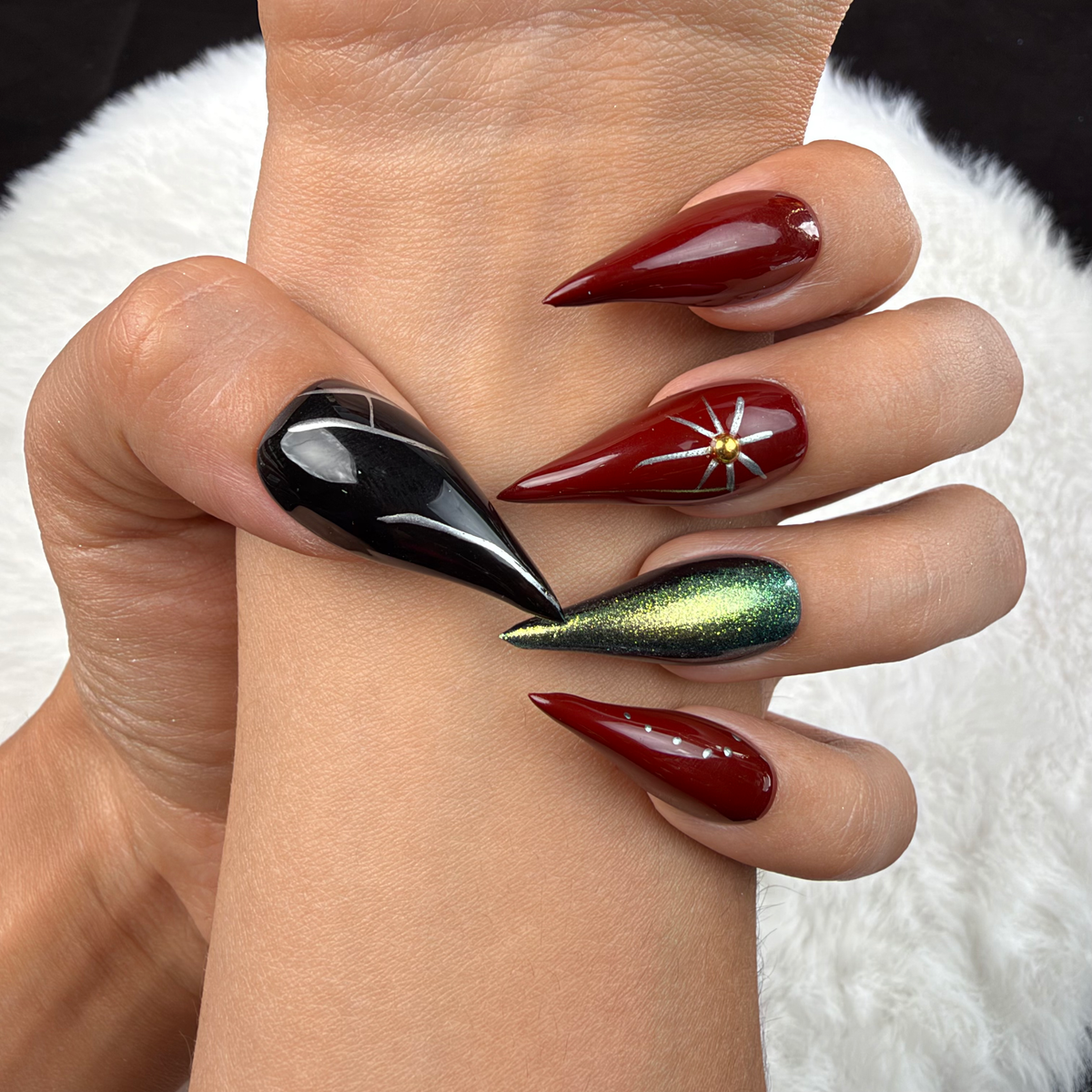 Close-up of hands wearing Ruby Orbit burgundy, green chrome and black star stiletto press-on nails