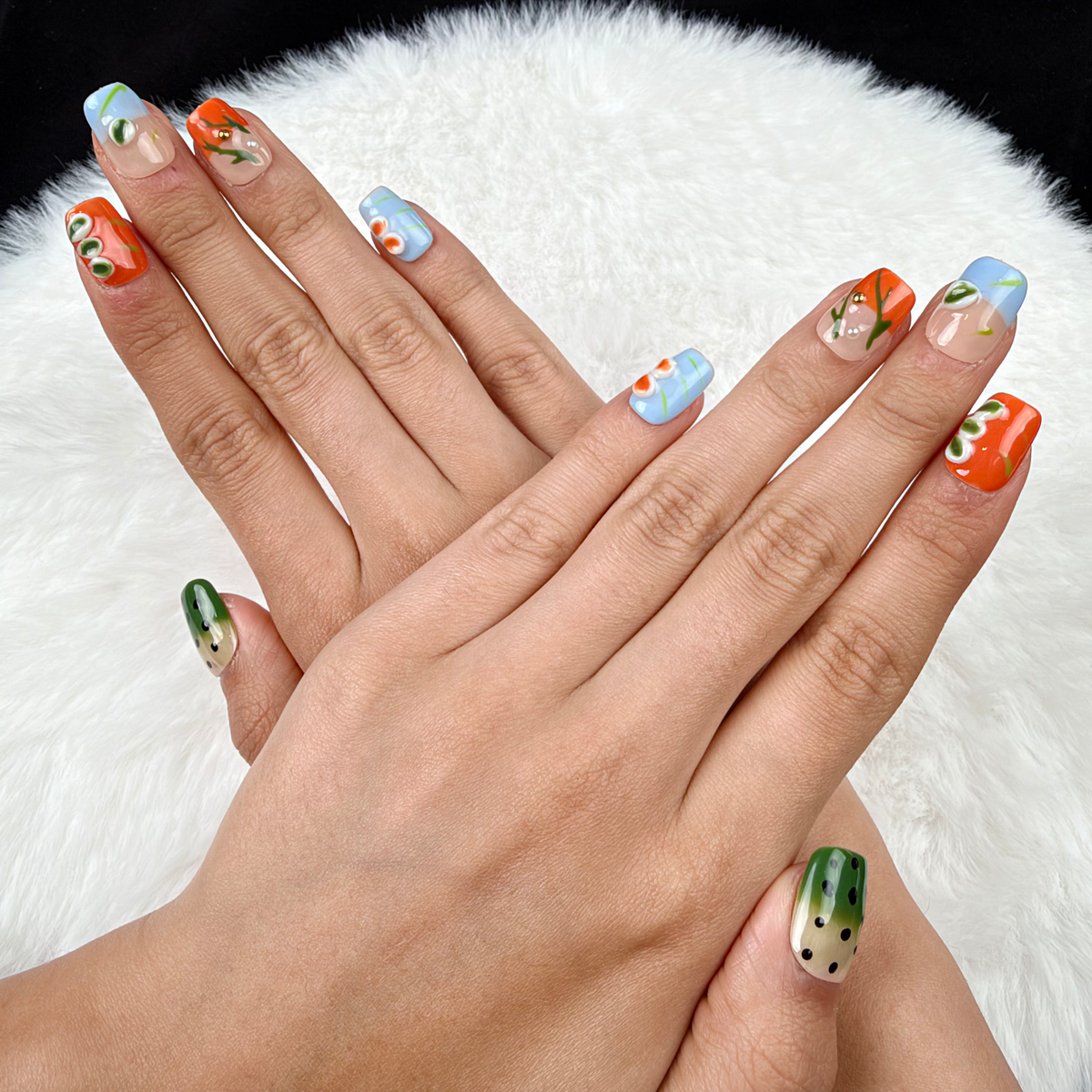 Hands wearing Summer Orchard orange, blue and green floral square press-on nails