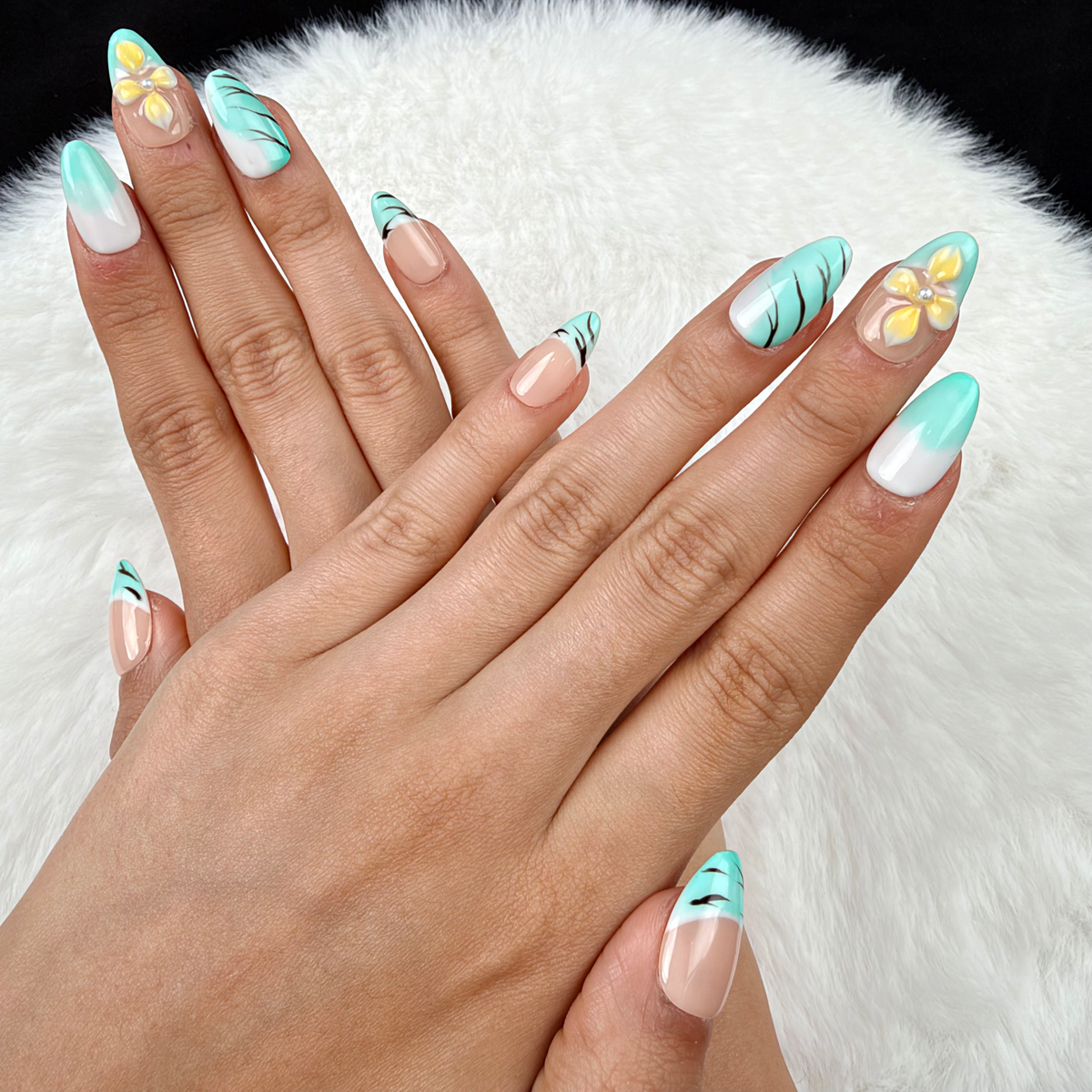 Hands wearing Mint Breeze mint French tip and yellow floral almond press-on nails