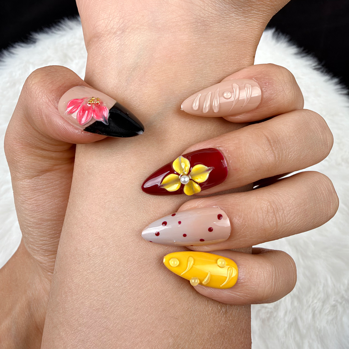 Detail shot of Golden Orchid yellow, burgundy and black floral almond press-on nails on hand