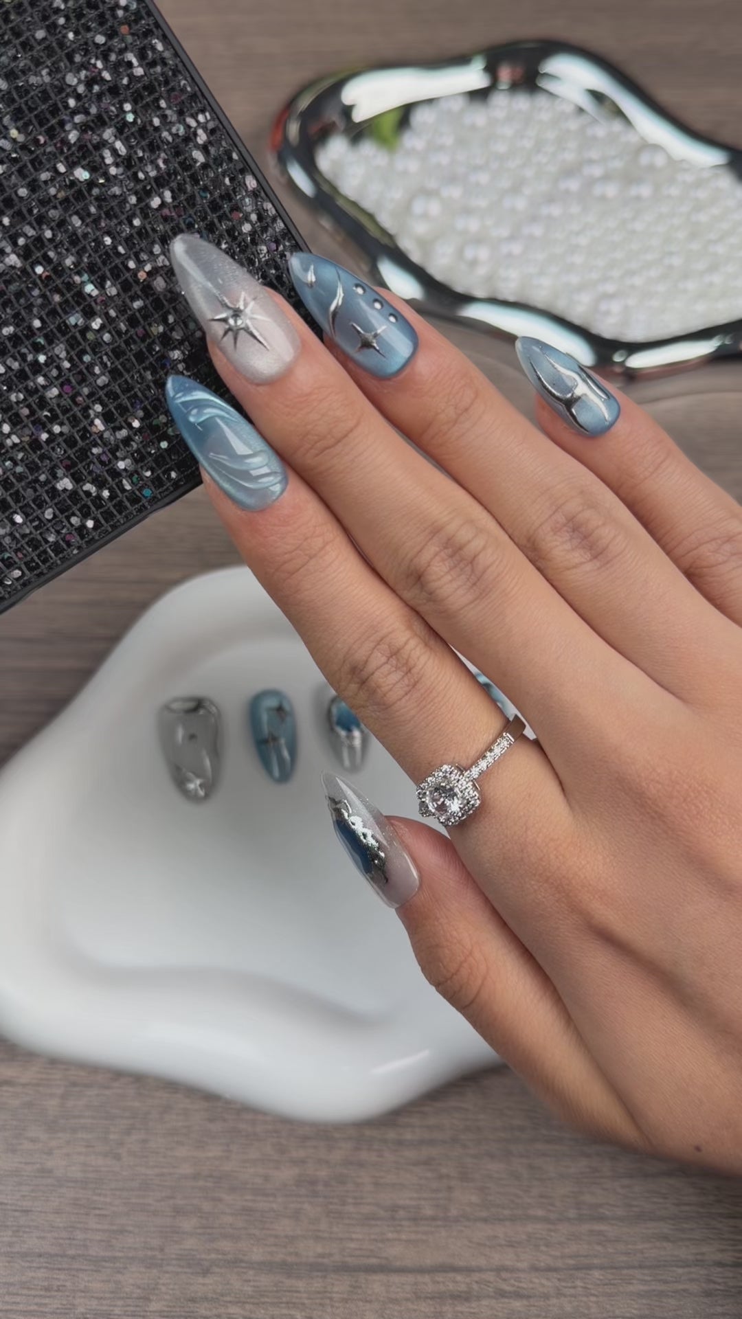 Load video: Step-by-step application of Blue Orbit icy blue cat eye celestial almond press-on nails with silver details