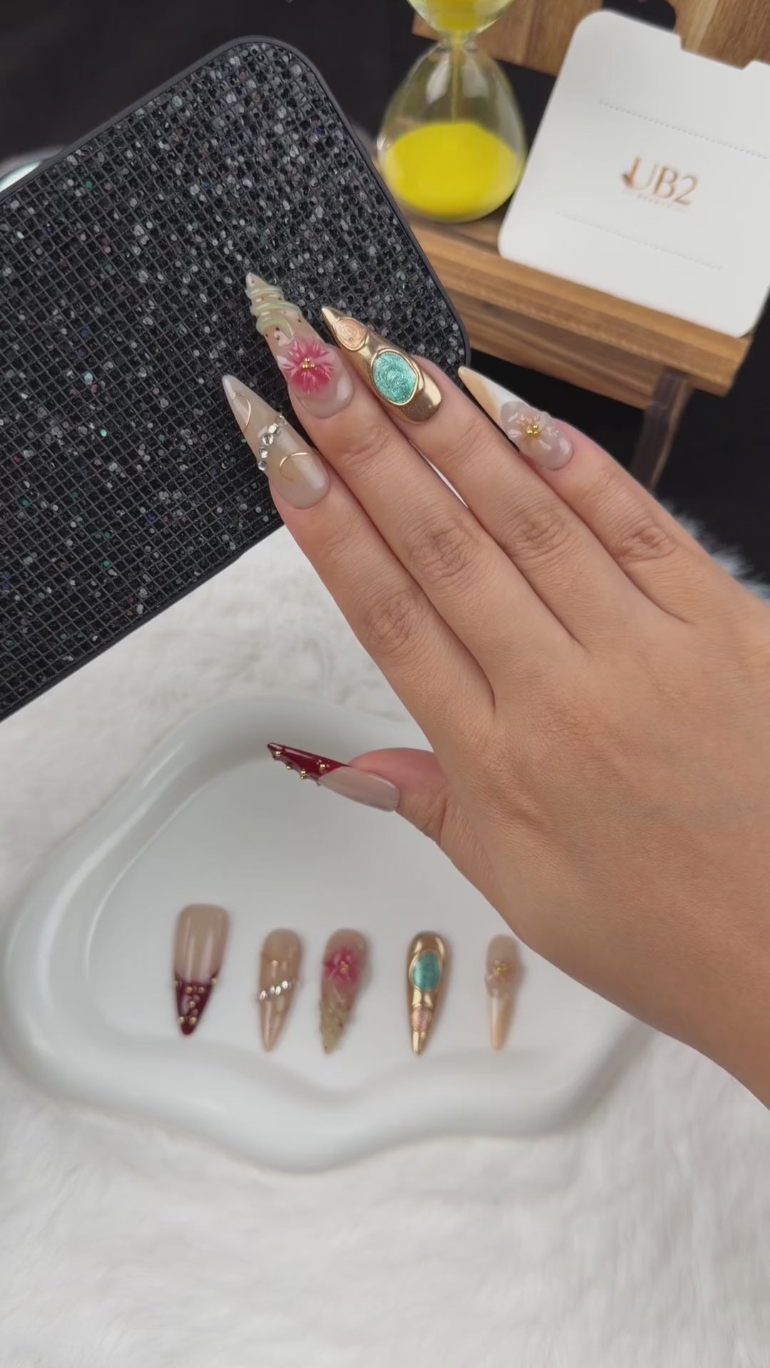 Load video: Step-by-step application of Gilded Garden nude, burgundy and turquoise floral almond press-on nails with gold accents