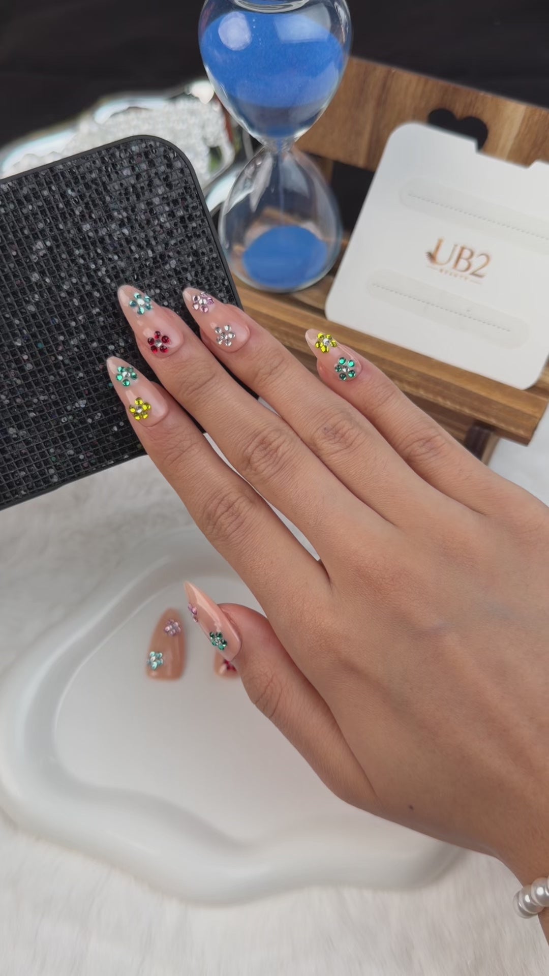 Load video: Step-by-step application of Sticker Party nude pink medium almond press-on nails with colorful rhinestone flowers